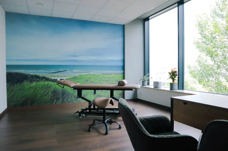 Gabinet z widokiem na zieleń za oknem — stół terapeutyczny i fototapeta